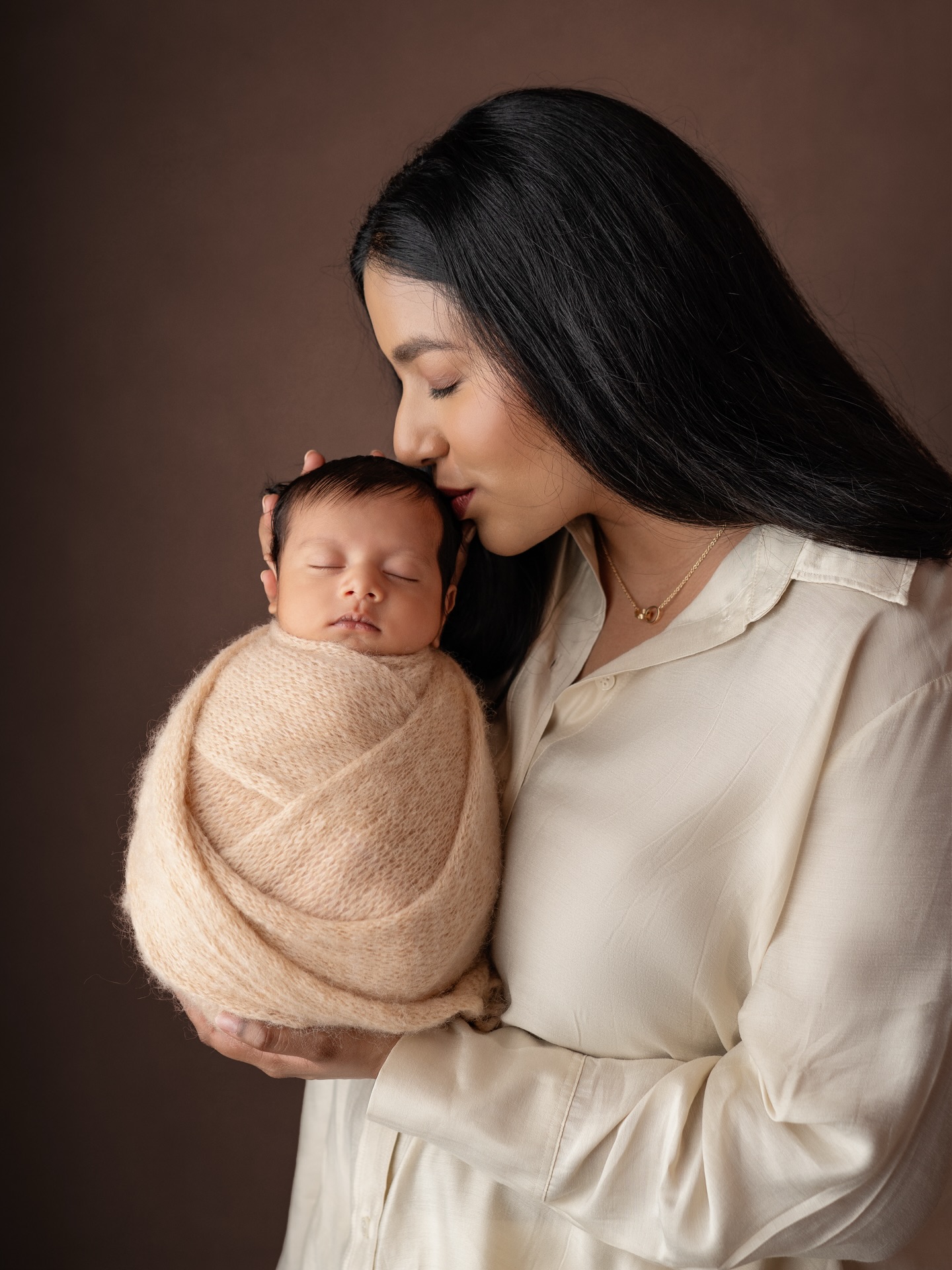 A mother holding her wrapped newborn, by Nivetha Photography